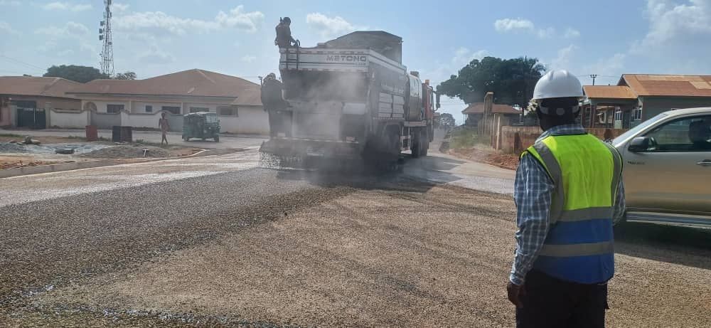 Road construction with workers and machinery spreading asphalt on a street under clear skies.